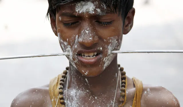 An Indian devotee, with a steel trident pierced through his cheeks as part of a ritual, participates in a religious procession to the temple of Hindu goddess Muthumariamman in Mumbai, India, Saturday, March 28, 2015. The devotees perform the ritual after their prayers to the goddess have been answered or their wishes fulfilled. (Photo by Rajanish Kakade/AP Photo)