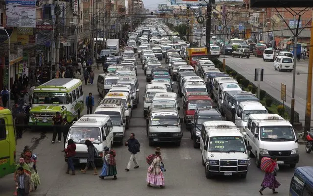 In this December 9, 2013 photo, traffic at a standstill as pedestrians cross a street in El Alto, Bolivia. The Bolivian highlands' city has hired Aymara women dressed in traditional multi-layered Andean skirts and brightly embroidered vests to work as traffic cops and bring order to its road chaos. (Photo by Juan Karita/AP Photo)