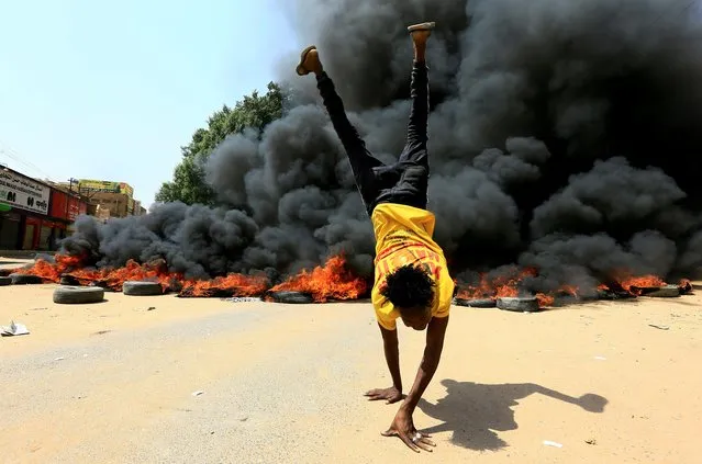 A person does a handstand in front of a burning pile of tyres during a protest against prospect of military rule in Khartoum, Sudan on October 21, 2021. (Photo by Mohamed Nureldin Abdallah/Reuters)