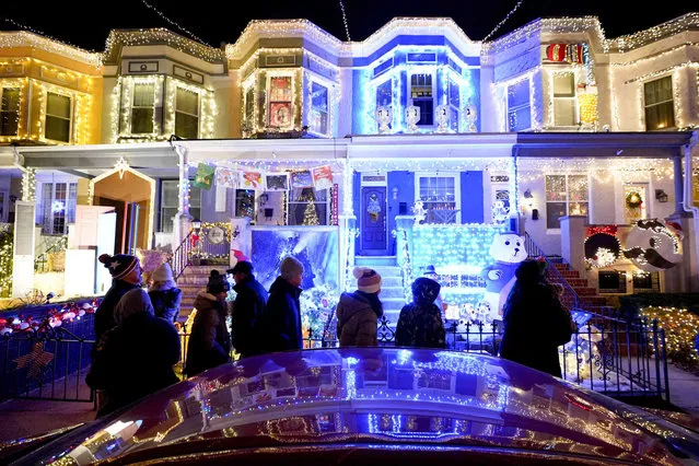 People walk in front of row homes covered in holiday decorations along the Miracle on 34th Street Hampden Christmas Street Holiday Show, Thursday, December 9, 2021, in the Hampden neighborhood of Baltimore. (Photo by Julio Cortez/AP Photo)