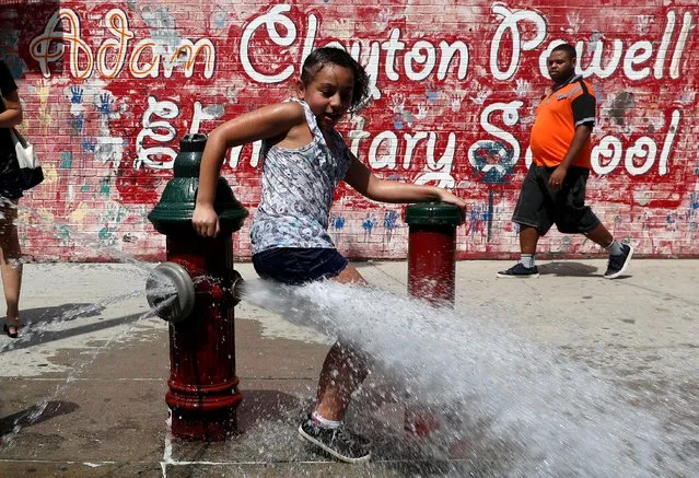 A girl cools off from the heat in water from an open fire hydrant in the Washington Heights section of upper Manhattan in New York City, New York, U.S., July 19, 2019. (Photo by Mike Segar/Reuters)
