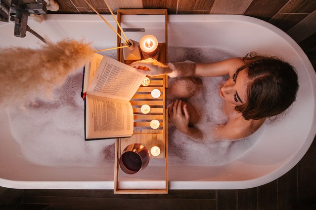 High angle view of a young woman reading in a bathtub, turning page, enjoying time with herself. Candles and red wine. Valentines day concept, International womans day. (Photo by Vuk Saric/Getty Images)