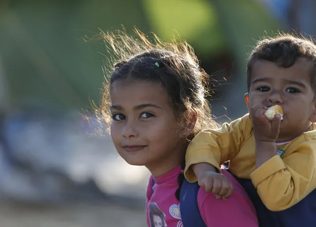 Sema el Husein, from Syria carries her brother Yamin as they walk amongst tents, at the makeshift camp at the northern Greek border point of Idomeni, Greece, Monday, April 11, 2016. More than 12,000 people have been stuck her for more than a month amid hopes that the border would reopen. (Photo by Amel Emric/AP Photo)