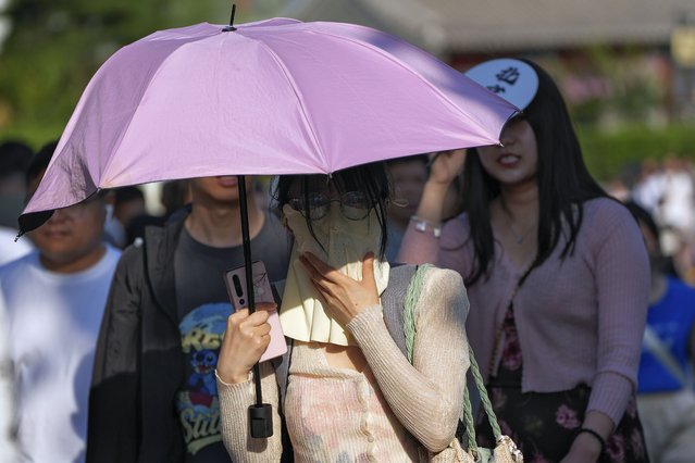 A woman wearing a face cover carrying an umbrella walks among the crowd in a hot and sunny day in Beijing, Sunday, June 16, 2024. (Photo by Andy Wong/AP Photo)