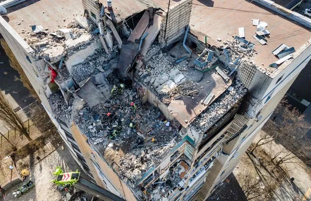 An aerial view shows firemen working in the rubble of a residential building which was hit by the debris from a downed rocket in Kyiv on March 17, 2022. (Photo by Fadel Senna/AFP Photo)