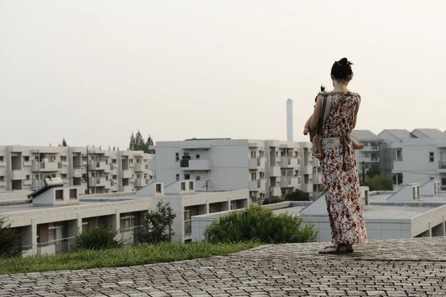 A woman holding a baby looks out over the Tama New Town residential development in Tama City, Tokyo, Japan, on Tuesday, August 13, 2013. (Photo by Akio Kon/Bloomberg)