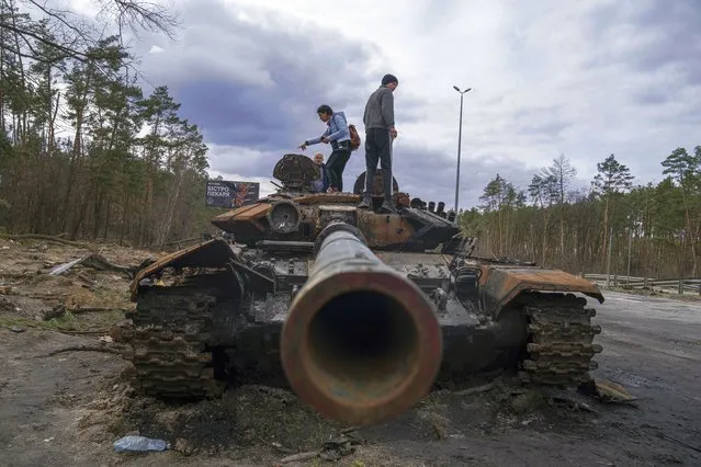 Local residents stand atop of a Russian tank damaged during fightings between Russian and Ukrainian forces in the outskirts of Kyiv, Ukraine, Monday, April 11, 2022. (Photo by Evgeniy Maloletka/AP Photo)
