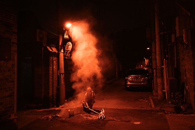 A woman burns offerings for her dead ancestors on a street during the Hungry Ghost Festival in Beijing on August 18, 2024. The festival is celebrated in the seventh lunar month of the lunar new year calendar among communities in southern China, Malaysia, Singapore, Hong Kong and Taiwan, marks the belief that the “Gates of Hell” are opened to let out the hungry ghosts who then wander in the land of the living while foraging for food. During the festival food offerings are made while paper money and joss sticks are burnt outside homes to keep the spirits of dead ancestors happy and to bring good luck. (Photo by Pedro Pardo/AFP Photo)