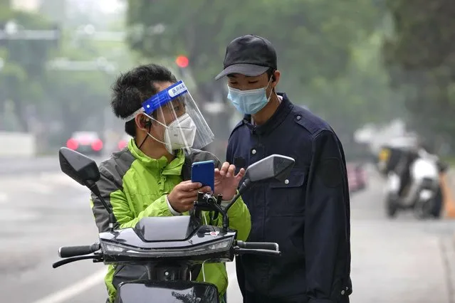 A delivery worker wearing a face shield and a mask asks for a direction from a security guard near a shuttered mall in the central business district on Tuesday, May 10, 2022, in Beijing. (Photo by Ng Han Guan/AP Photo)