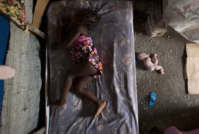 In this June 26, 2015 photo, two-year-old Naika Pierre sleeps on a bed in the dirt-floor tent where she lives with her parents in one of the remaining post-earthquake camps in Cite Soleil, Port-au-Prince, Haiti. When the earthquake struck in 2010, the building where Naika's parents were living in Cite Soleil was heavily damaged and they were forced to move into a tent camp inside the slum. Five years later, they are still living under pieced-together tarps, with cardboard and cinderblocks, the only buffer from a dirt floor that can turn to mud in the rains. (Photo by Rebecca Blackwell/AP Photo)