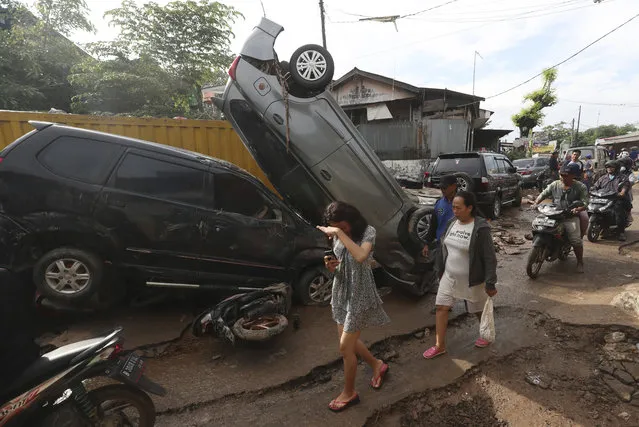 Residents walk near the wreckage of cars that were swept away by flood in Bekasi, West Java, Indonesia, Friday, January 3, 2020. Severe flooding in greater Jakarta has killed scores of people and displaced tens of thousands others, the country's disaster management agency said. (Photo by Achmad Ibrahim/AP Photo)