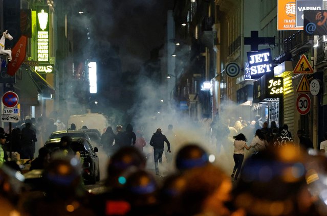 Demonstrators run as French police officers use tear gas in Paris on July 2, 2023, five days after a 17-year-old man was killed by police in Nanterre, a western suburb of Paris. French police arrested 1311 people nationwide during a fourth consecutive night of rioting over the killing of a teenager by police, the interior ministry said on July 1, 2023. France had deployed 45,000 officers overnight backed by light armoured vehicles and crack police units to quell the violence over the death of 17-year-old Nahel, killed during a traffic stop in a Paris suburb on June 27, 2023. (Photo by Ludovic Marin/AFP Photo)