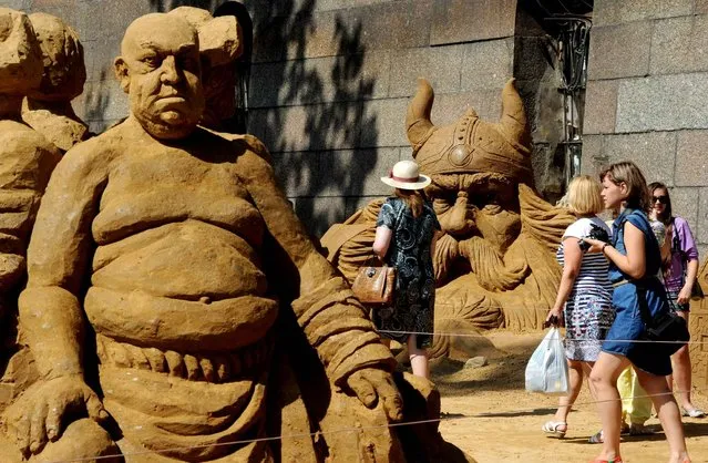 Visitors walk past sand sculptures displayed during the 13th International Festival of sand sculptures World of fairy tales in the Peter and Paul Fortress in St.Petersburg on July 17, 2014. (Photo by Olga Maltseva/AFP Photo)