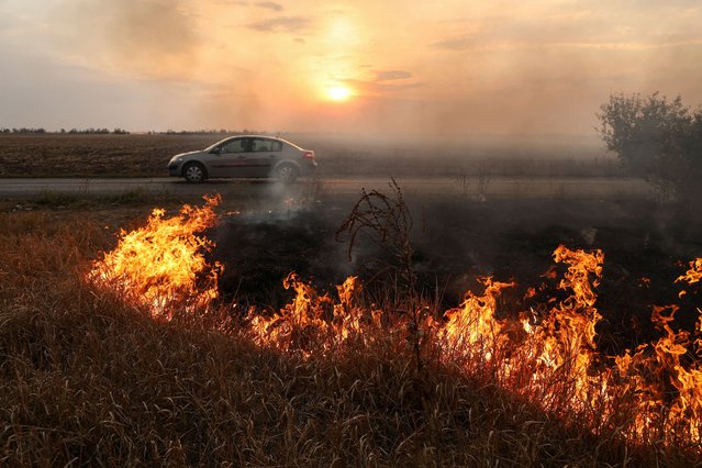 A person drives a car along a road while roadside burns after a Russian military strike outside the town of Pokrovsk, in Donetsk region, Ukraine on September 17, 2024. (Photo by Anton Shynkarenko/Reuters)