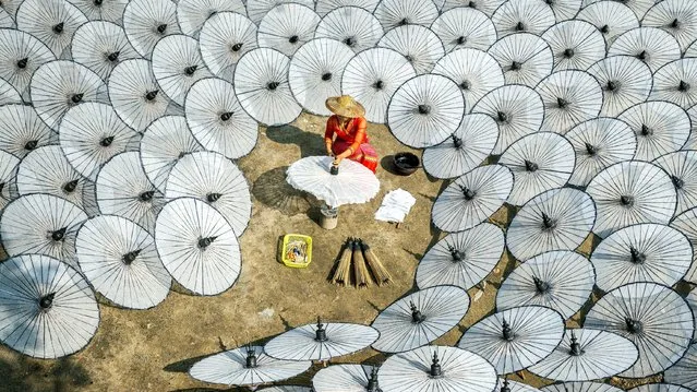 A woman in Myanmar makes an umbrella in January 2022. The painted cotton parasols are left to dry under the sun before being decorated. (Photo by Zay Yar Lin/Solent News)