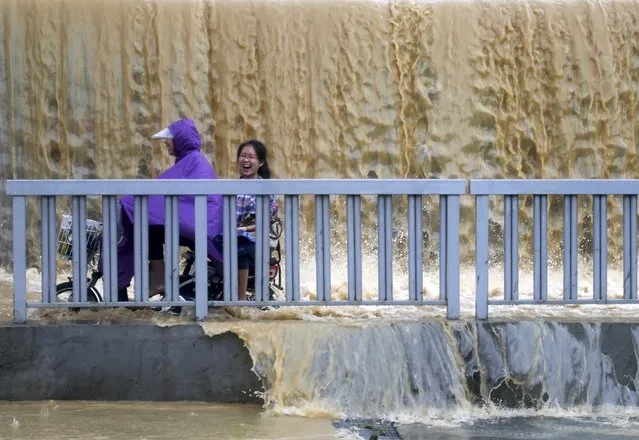 A woman laughs as she sits on the back of an electric bicycle while riding through a flooded street in Fuzhou, Fujian province, July 23, 2014. Typhoon Matmo hit Taiwan on Wednesday, bringing heavy rain and strong winds, shutting financial markets and schools. It passed the island and headed into China, downgraded from typhoon to tropical storm. (Photo by Reuters/Stringer)