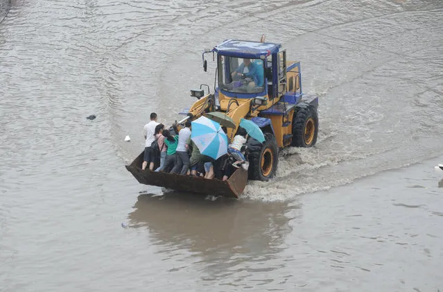Residents ride on a heavy machinery at a flooded area in Taiyuan, Shanxi Province, China, July 20, 2016. (Photo by Reuters/Stringer)