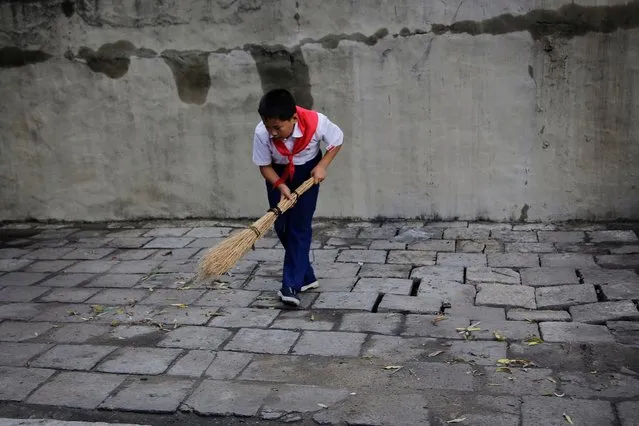 A school boy sweeps a sidewalk in Pyongyang, North Korea on July 28, 2017. (Photo by Wong Maye-E/AP Photo)