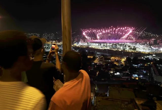 2016 Rio Olympics, Opening Ceremony, Maracana, Rio de Janeiro, Brazil on August 5, 2016. People watch fireworks explode over the Maracana from the roof of their home in the Mangueira favela, or slum, as the Olympic opening ceremony unfolds. (Photo by Ricardo Moraes/Reuters)