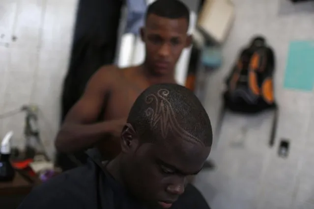 A youth has a design cut into his hair at the Barbearia Kengao (barber shop) in a slum in Rio de Janeiro September 6, 2014. According to Leandro, a barber and owner of the Barbearia Kengao, who charges about $7 for a haircut, business is good as young men from the slums often regard their hairstyles as a status symbol and sometimes get their hair styled up twice in a good-paying month. (Photo by Pilar Olivares/Reuters)
