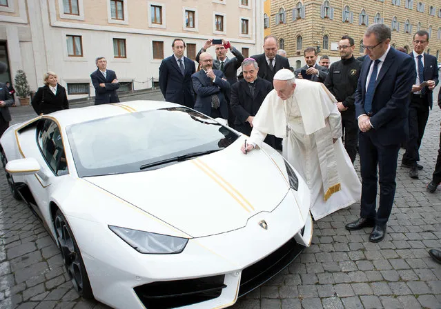 Pope Francis writes on the bonnet of a Lamborghini donated to him by the luxury sports car maker, at the Vatican, Wednesday, November 15, 2017. The car will be auctioned off by Sotheby's, with the proceeds going to charities including one aimed at helping rebuild Christian communities in Iraq that were devastated by the Islamic State group. (Photo by L'Osservatore Romano/Pool Photo via AP Photo)