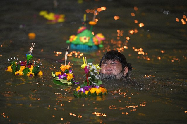 A boy swims in Chao Phraya River as he helps to place a Krathong, or a “floating basket”, in the water amid a yearly festival during which rafts of neatly folded banana leaves, decorated with flowers, candles and incense, are offered to thank the water goddess for good luck and for using her water to grow crops and support all life, in Bangkok, Thailand on November 8, 2022. (Photo by Chalinee Thirasupa/Reuters)