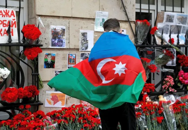 A man holding the national flag of Azerbaijan stands next to a makeshift memorial for people killed in the country during the military conflict over the breakaway region of Nagorno-Karabakh, outside the embassy of Azerbaijan in Moscow, Russia on October 19, 2020. (Photo by Evgenia Novozhenina/Reuters)