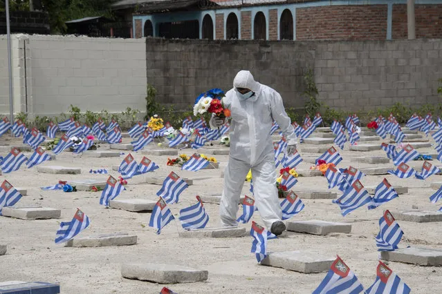 A municipal worker wearing a biosecurity suit carries flowers previously delivered by a relative of a victim of COVID-19, to be placed on his grave at La Bermeja cemetery during Day of the Dead in San Salvador on November 2, 2020. The municipality restricted access of relatives of victims of COVID-19 to place flowers on their graves. (Photo by Yuri Cortez/AFP Photo)