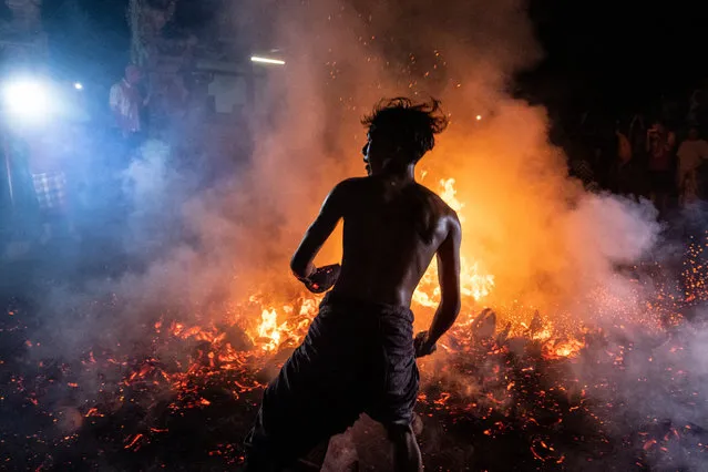 Balinese man runs in the middle of burn coconut husks during the fire fight ritual called Mesabatan Api on March 21, 2023 at traditional sub village of Nagi, in Gianyar, Bali, Indonesia. The mesabatan api ritual is held annually on the eve of Nyepi, the Hindu Day of Silence, the Balinese Caka New Year, and only takes place in Pakraman Nagi village in Gianyar regency, around 30 kilometers from Denpasar. (Photo by Agung Parameswara/Getty Images)