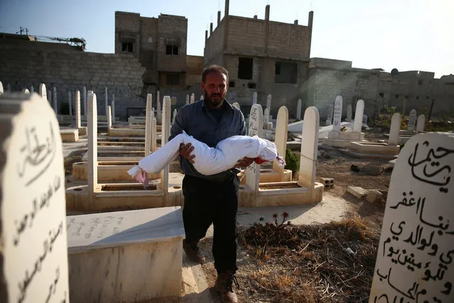 A man carries the body of dead child wrapped with cloth prior to burial in a graveyard after shelling in the rebel held besieged town of Douma, eastern Ghouta in Damascus, Syria, October 24, 2016. (Photo by Bassam Khabieh/Reuters)
