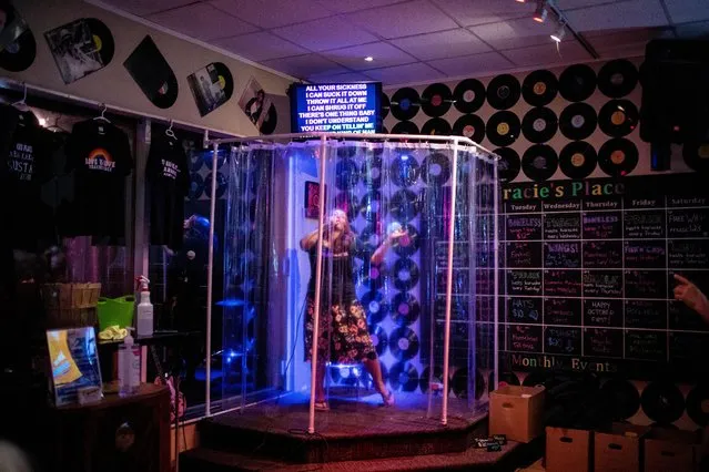 Bar owner Tracie England sings inside a makeshift “shower stall”, set up in order to protect patrons from the coronavirus at Tracie's Place Restaurant and Karaoke in Hamilton, Ontario, Canada October 2, 2020. The karaoke bar is letting its customers sing in the shower during the pandemic – to keep people safe, they've constructed a shower stall on stage, complete with curtains and tubular piping. (Photo by Carlos Osorio/Reuters)