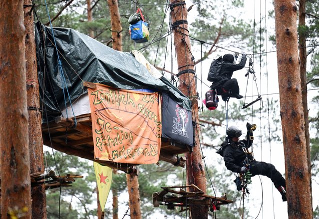 A German police officer and an activist are pictured in a protest camp where activists set up tree houses in a forest to protest against the expansion of the Tesla Gigafactory in Gruenheide near Berlin, Germany, on November 19, 2024. (Photo by Annegret Hilse/Reuters)