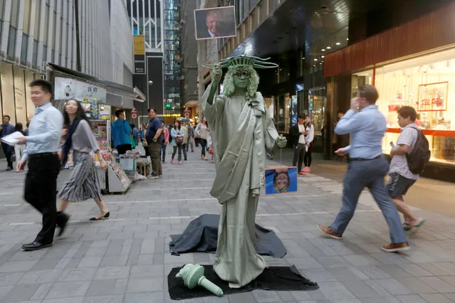 A street performer dressed as the Statue of Liberty hold photos of U.S. presidential candidates Donald Trump and Hillary Clinton at the financial Central district in Hong Kong, China November 9, 2016, after Trump won the presidency. (Photo by Bobby Yip/Reuters)