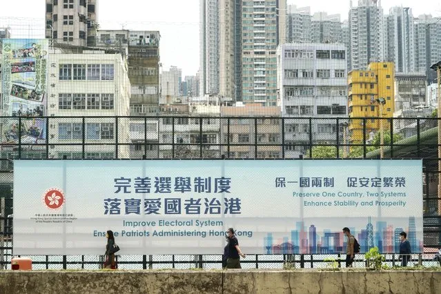 People walk past a government advertisement to promote the new Hong Kong electoral system reform, in Hong Kong, March 30, 2021. China's top legislature approved amendments to Hong Kong's constitution on Tuesday that will give Beijing more control over the make-up of the city's legislature. (Photo by Kin Cheung/AP Photo)