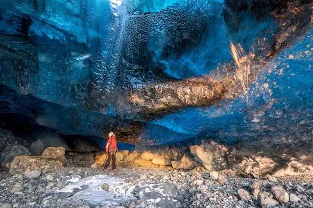 Stunning images have revealed ice-cool British tourists chilling out inside Europe’s largest glacier – despite being at risk of flooding. The spectacular collection of images show the explorers braving the freezing temperatures to climb, photograph and even abseil down the inside of the icy cliff sides. Another image shows one visitor on his knees appearing to pray next to a water fall of melted ice. Other glistening shots show an adventurer trying to keep warm by a fire whose flames dance beautifully against the glossy roof. More shots show the caves sparkling like crystal with one ice formation appearing to resemble bubble wrap. In one picture, a brave tourist stands at the edge of a river flowing through the centre of the frosty caves. (Photo by Einar Runar Sigurdsson/Mediadrumworld.com)