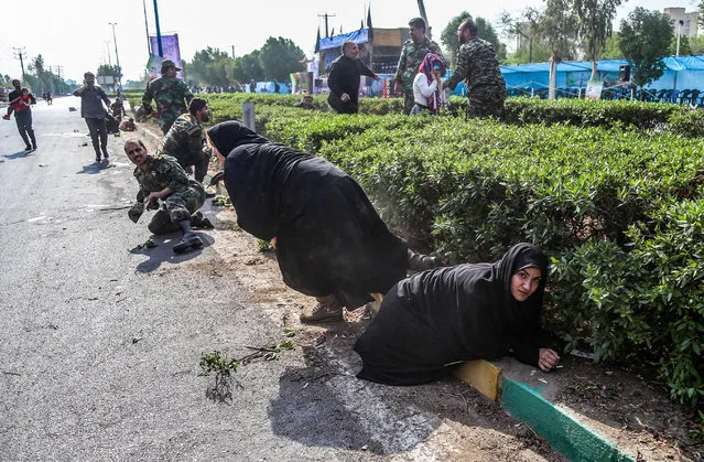This picture taken on September 22, 2018 in the southwestern Iranian city of Ahvaz shows Iranian women and soldiers taking cover next to bushes at the scene of an attack on a military parade that was marking the anniversary of the outbreak of its devastating 1980-1988 war with Saddam Hussein's Iraq. Dozens of people were killed with dozens others wounded in an attack in the southwestern Khuzestan province on September 22 targeting on an army parade commemorating the anniversary of the 1980-1988 Iran Iraq war, state media reported. (Photo by Morteza Jaberian/AFP Photo)