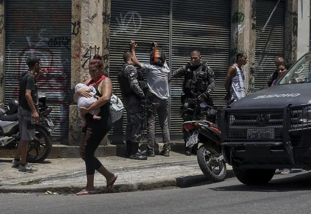 A woman carries a baby as she walks past police searching several men, during an operation targeting drug traffickers in the Santa Teresa neighborhood of Rio de Janeiro, Brazil, Friday, February 8, 2019. Law enforcement officials in Brazil's second largest city say that at least 11 suspected drug traffickers were killed in a shootout with police in a slum located in the bohemian Santa Teresa neighborhood. (Photo by Carson Gardiner/AP Photo)