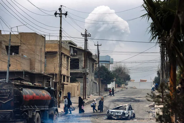 Iraqis walk down a street while smoke rises in the background following a car bomb explosion in eastern Mosul, on January 15, 2017, during an ongoing military operation by security forces against Islamic State (IS) group jihadists. Iraqi forces on January 14 retook Mosul's university from the Islamic State jihadist group, the latest key advance in efforts to recapture the eastern side of the city, officers said. (Photo by Dimitar Dilkoff/AFP Photo)