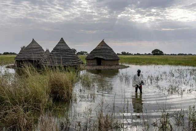 Yel Aguer Deng, who does not know his age, walks through water from his compound to the Wanyhok-Akon road, near Malualkon in Northern Bahr el Ghazal State, South Sudan, Wednesday, October 20, 2021. The worst flooding that parts of South Sudan have seen in 60 years now surrounds his home of mud and grass. His field of sorghum, which fed his family, is under water. Surrounding mud dykes have collapsed. The United Nations says the flooding has affected almost a half-million people across South Sudan since May. (Photo by Adrienne Surprenant/AP Photo)