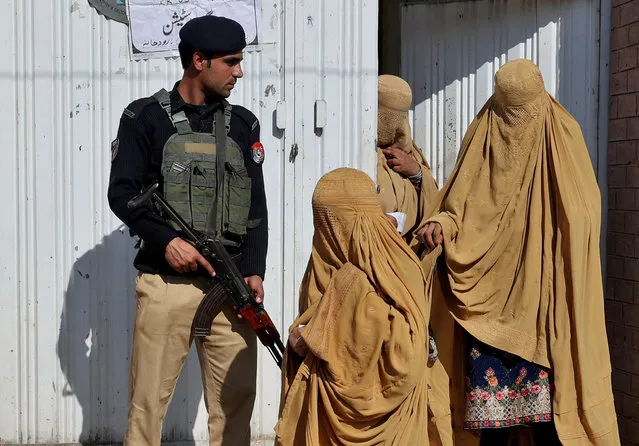 Burqa-clad women leave a polling station after casting their vote as a police officer stands guard during general election, in Peshawar, Pakistan on February 8, 2024. (Photo by Fayaz Aziz/Reuters)