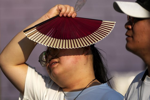 A woman uses a fan to block from the sun as she walks with her companion in an unseasonably hot day in Beijing, Sunday, June 16, 2024. China is being buffeted by two weather extremes, with heavy rain and flooding in parts of the south and a heat wave and potential drought in the north. (Photo by Andy Wong/AP Photo)
