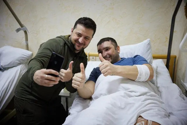 In this handout picture released and taken by Ukrainian Presidency Press Office on March 13, 2022, Ukrainian President Volodymyr Zelensky (L) snaps a selfie with an injured man laying on a bed during a visit at a military hospital following fightings in the Kyiv region. According to the presidency official website, Zelensky made a visit to the hospital to “award militaries with orders and medals for courage and dedication, and to honor the hospital staff for exemplary work in difficult conditions”. (Photo by Handout/Ukrainian Presidential Press Service/AFP Photo)
