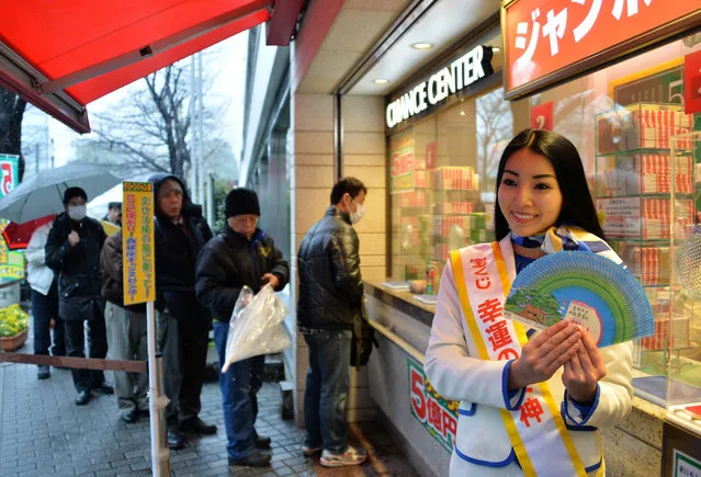 Campaign girl Miku Ishitani (R) displays sample lottery tickets as people (background) queue up to purchase tickets for the “Green Jumbo Lottery” as the first tickets go on sale in Tokyo on February, 2014. Lotteries originated in Japan in the 1600s. They were banned and resurrected several times until being banned entirely in 1842. After more than a hundred years of absence, the Japanese love for gambling could no longer be restrained and lotteries were finally revived in 1945. Takara-kuji lotteries were used to rebuild the country and help stave off rapidly escalating inflation. (Photo by Yoshikazu Tsuno/AFP Photo)