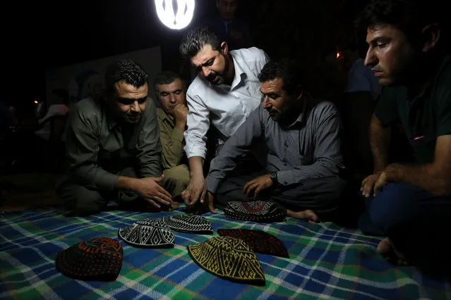 In this Tuesday, July 7, 2015 photo, Kurdish men discuss which hat to pick up while playing a game of Klawane in Irbil, Iraq. The traditional Iraqi Kurdish game is only played after Iftar during Ramadan. Two teams of four compete, where one team hides a ring in a traditional hat. The other team has to guess in which hat the ring is hidden. The team that hides the ring scores points for each hat that is leftover after the other team finds the ring. (Photo by Bram Janssen/AP Photo)