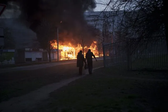 A couple of residents walk past burning shops after a Russian attack in Kharkiv, Ukraine, Monday, April 11, 2022. (Photo by Felipe Dana/AP Photo)