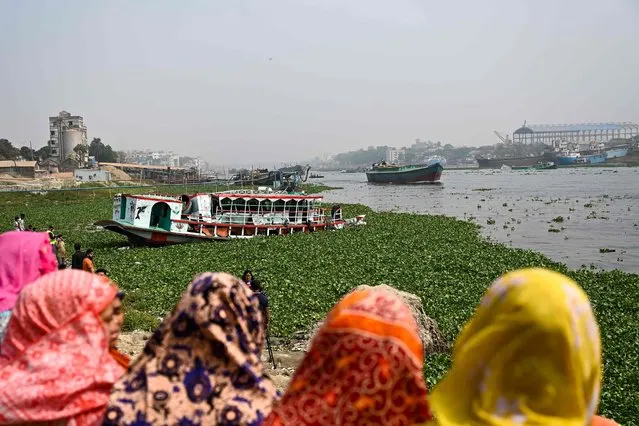 People watch the rescued ferry following an accident in the Shitalakshya River in Narayanganj on March 21, 2022. At least six people are dead and dozens more are believed missing after a bulk carrier crashed into a small ferry in a river near Bangladesh's capital on March 20. (Photo by Munir Uz Zaman/AFP Photo)
