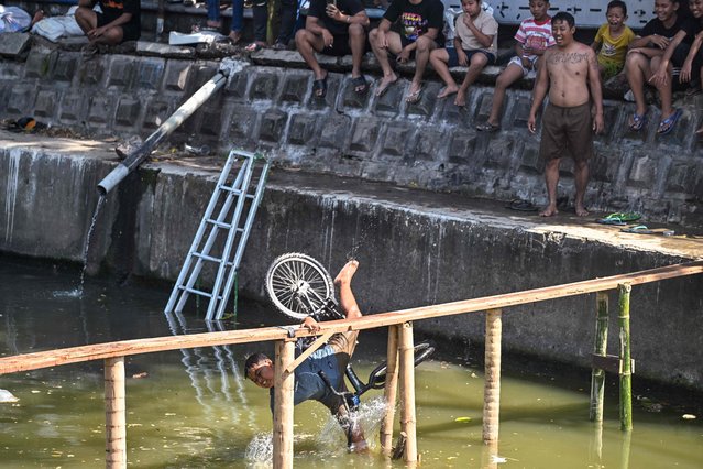 A child falls during a bicycle balance competition over a plank on a river, part of community festivities ahead of the 79th anniversary of Indonesia's Independence Day, in Surabaya on August 11, 2024. (Photo by Juni Kriswanto/AFP Photo)