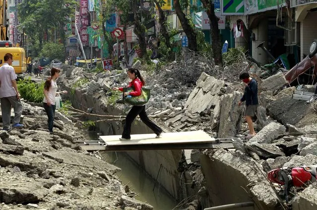 A woman crosses over a trench made from a massive gas explosion in Kaohsiung, Taiwan, Friday, August 1, 2014. Scores of people were killed and more than 200 others injured when several underground gas explosions ripped through Taiwan's second-largest city overnight, hurling concrete through the air and blasting long trenches in the streets, authorities said Friday. (Photo by Wally Santana/AP Photo)