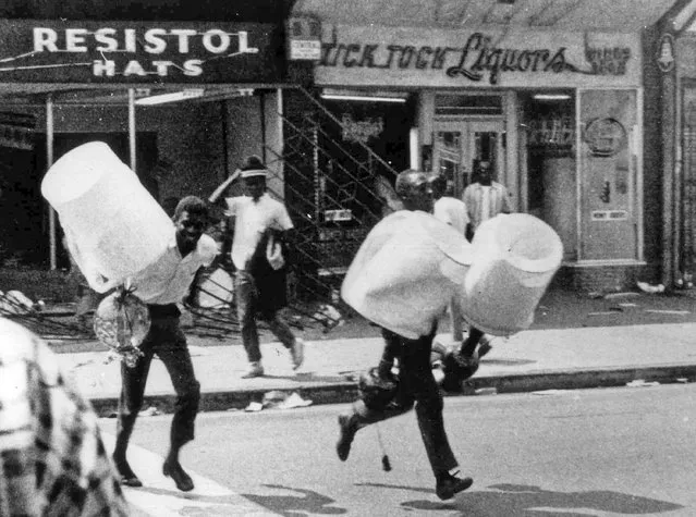 In this August 13, 1965 file photo, men carry items from a looted store during the rioting that enveloped the Watts district of Los Angeles. It began with a routine traffic stop 50 years ago this month, blossomed into a protest with the help of a rumor and escalated into the deadliest and most destructive riot Los Angeles had seen. The Watts riot broke out Aug. 11, 1965 and raged for most of a week. When the smoke cleared, 34 people were dead, more than a 1,000 were injured and some 600 buildings were damaged. (Photo by AP Photo)