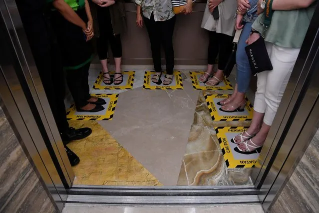 Visitors stand on boxes for social distancing inside an elevator at a shopping mall in Surabaya, East Java province, Indonesia, March 18, 2020. (Photo by Zabur Karuru/Antara Foto via Reuetrs)